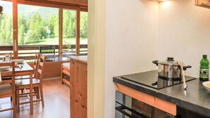 A wooden dining table with chairs, a kitchen counter with a stove, and a window overlooking a forest. - Rosablanche C22 by Interhome (Siviez-Nendaz)