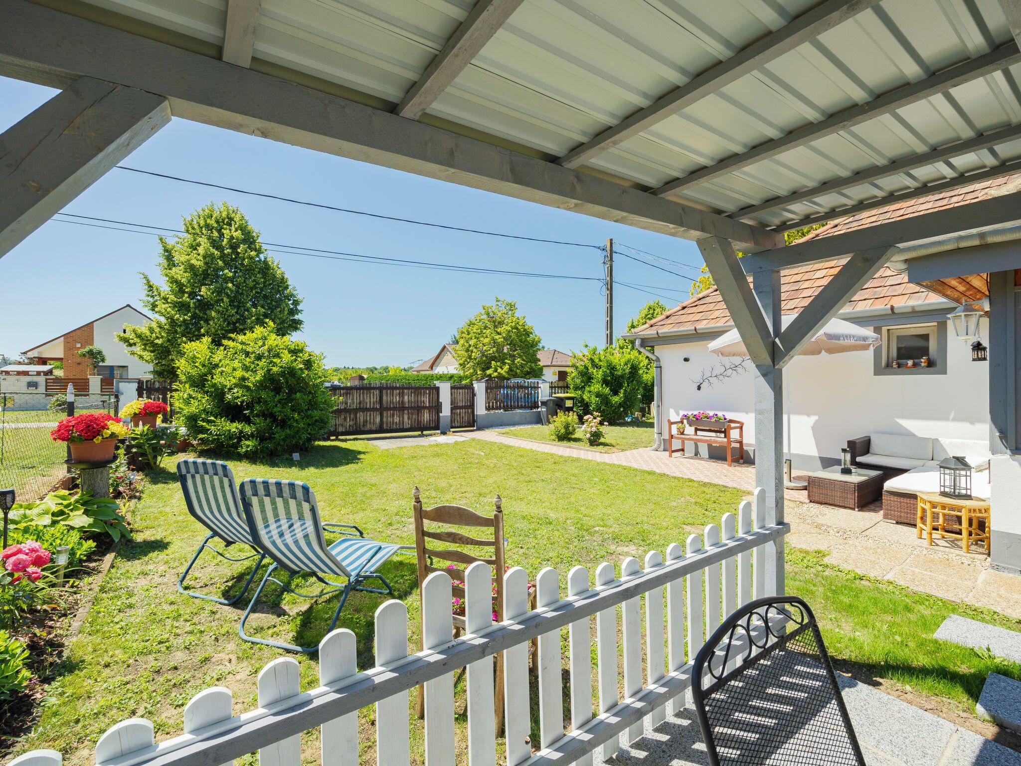 Un patio cubierto con cerca blanca de piquete, mobiliario exterior y vista a un barrio residencial.