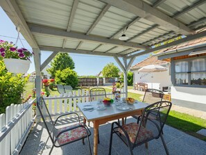 Eine überdachte Terrasse mit Esstisch, umgeben von Stühlen und einem weißen Ziergartenzaun.