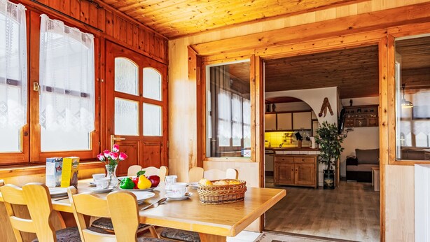 Een houten eethoek met een ontbijttafel, stoelen en uitzicht op de keuken.