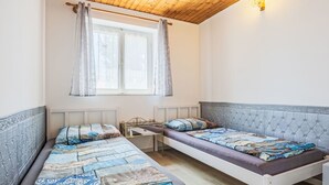 Een kamer met twee bedden, een klein tafeltje en een raam met gordijnen.