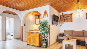 Een ruime woonkamer met houten vloer, een bank, een salontafel en een aan de muur bevestigde televisie.