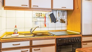 Een keuken met houten kastjes, een roestvrijstalen spoelbak, een fornuis en een rekje voor kruiden.