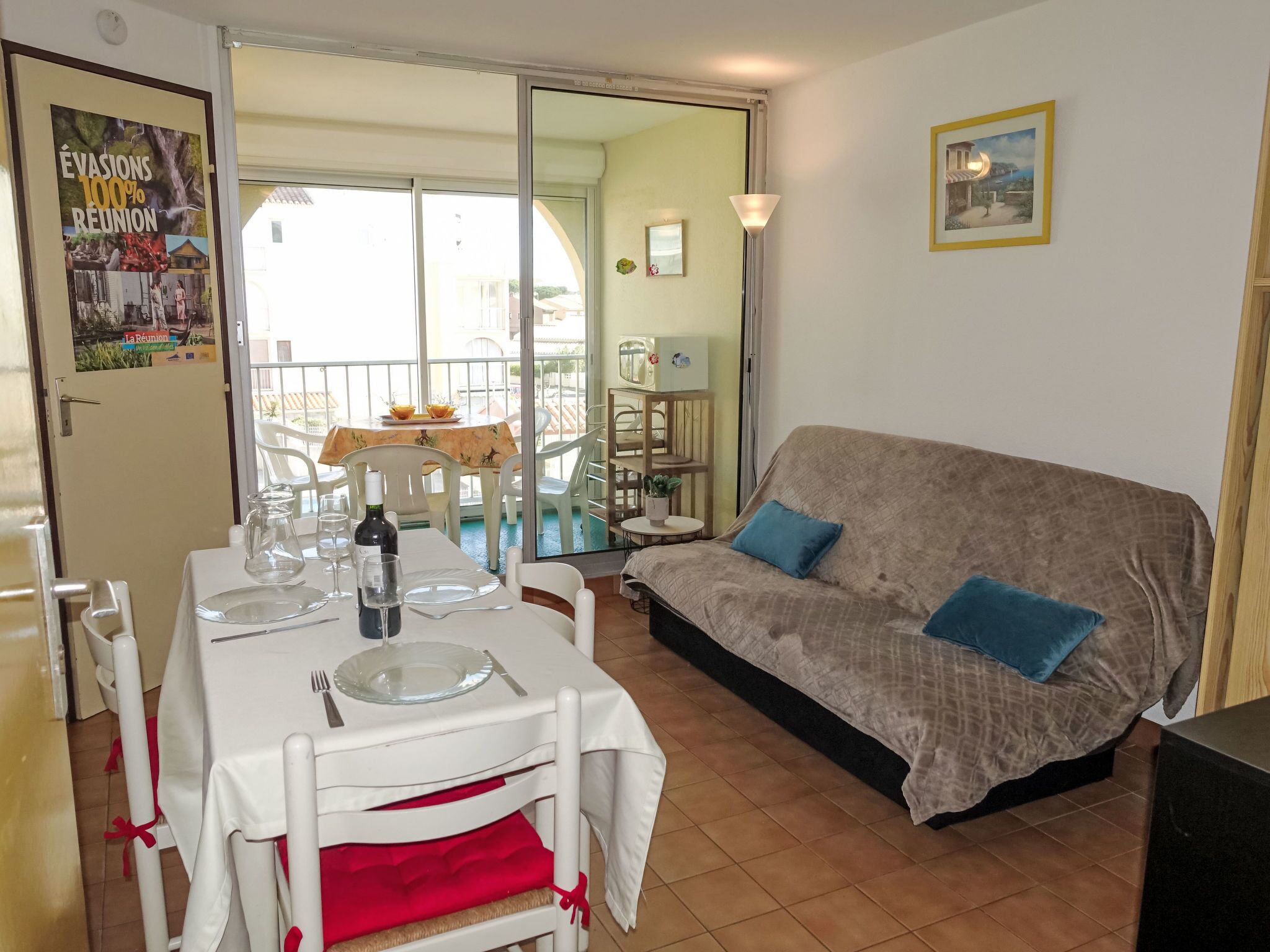 A dining area with a table set for two, a sofa, and a balcony with a table and chairs.