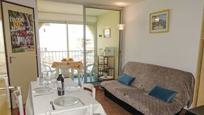Un coin repas avec une table dressée pour deux personnes, un canapé et un balcon équipé d’une table et de chaises.