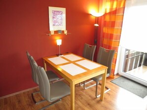 A dining area with a wooden table, four chairs, a framed picture on the wall, a floor lamp, and a window with curtains.