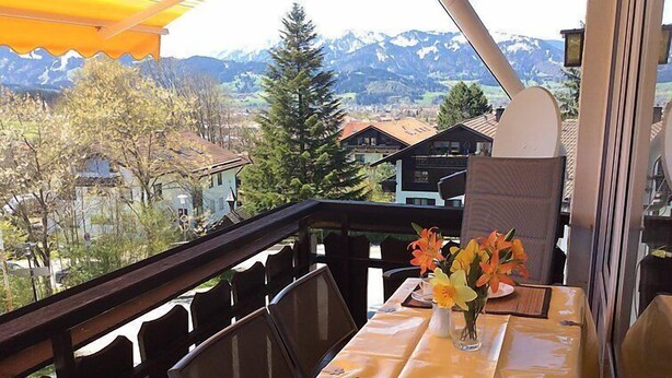 Ein Balkon mit Tisch für zwei Personen, mit Blick auf eine gebirgige Landschaft.