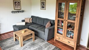 Ein Wohnzimmer mit grauem Sofa, einer Holzkombination mit Glastüren, einem kleinen Holztisch und einem grauen Teppich.
