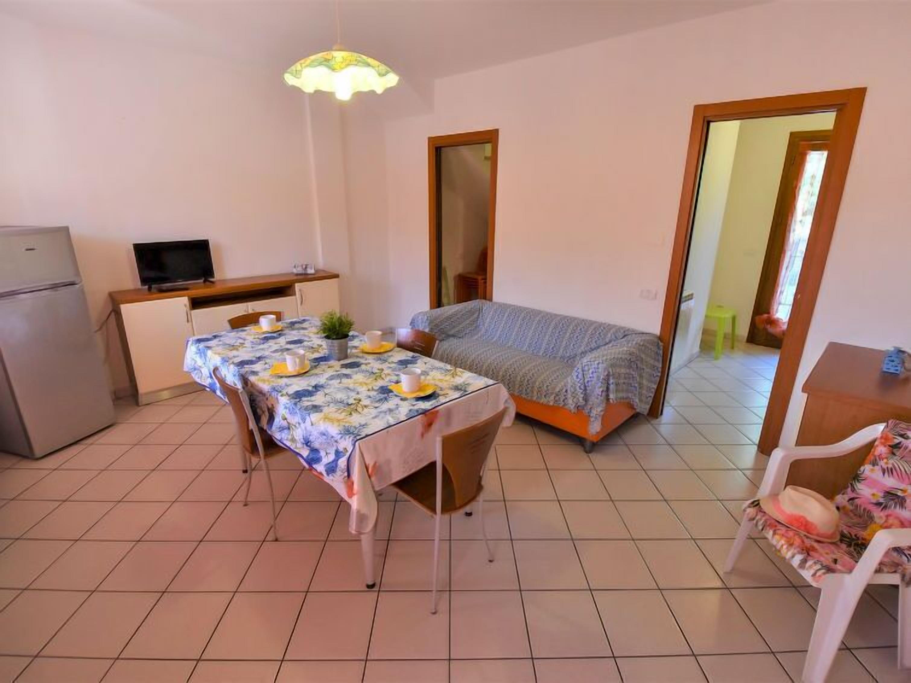 A compact room with a dining table set for two, a bed, a television, and a refrigerator.