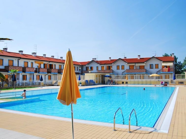 A swimming pool with a wooden deck, a yellow umbrella, and a row of houses in the background.