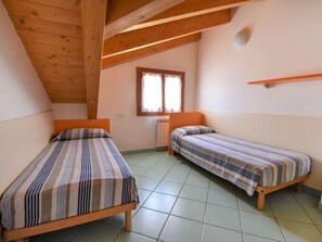 Una habitación pequeña y acogedora con dos camas individuales, vigas de madera en el techo, una ventana con cortinas y un radiador.