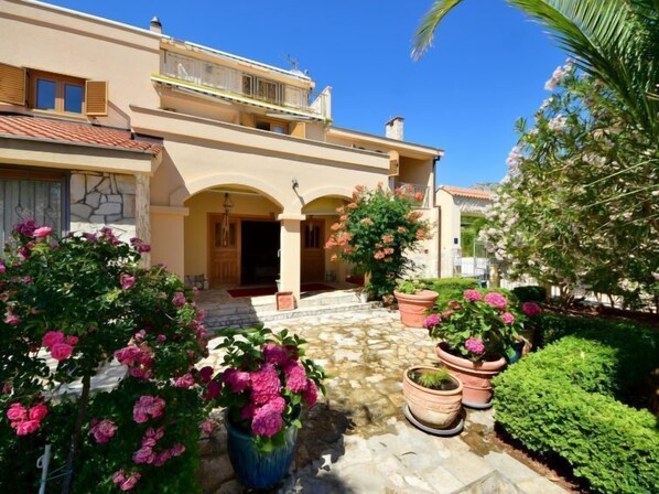 A Mediterranean-style villa with a stone courtyard, potted plants, and a clear blue sky.