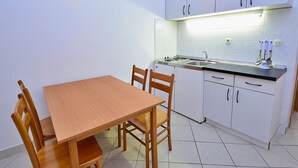 A small kitchen with white cabinets, a wooden dining table, and chairs. There is a stove, sink, and a wall-mounted light fixture. - Meridiana by Interhome (Orebic)