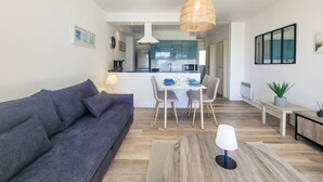 Ein modernes Wohnzimmer mit grauem Sofa, einem Esstisch mit Stühlen, einer Pendelleuchte und einer Küche im Hintergrund.