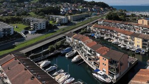 A marina with boats docked, surrounded by residential buildings with red-tiled roofs, and a mountainous backdrop.