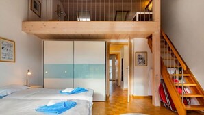 A hotel room with two beds, a wooden ceiling, a staircase, and a hallway leading to other rooms.