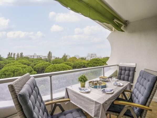 Un balcón con una mesa preparada para dos, sillas y vistas a un paisaje verde con edificios al fondo.