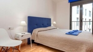 A bedroom with a bed, a nightstand, a chair, and a window with a view of buildings. - Escorxador by Interhome (Colera)