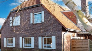 A two-story brick house with white shutters, a wooden fence, and a clear sky. - Küstennebel by Interhome (Norddeich)