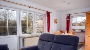 A modern living room with a dark blue sofa, a dining table with chairs, and large windows with red curtains. - Küstennebel by Interhome (Norddeich)