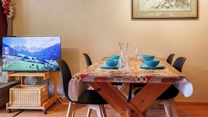 A dining area with a table set for four, a television on a stand, and a framed artwork on the wall. - Dents Rousses H2 by Interhome (Siviez-Nendaz)