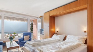 A hotel room with a bed, a chair, a small table, and a view of the outside. - Promenade Apt 306 by Interhome (Arosa)