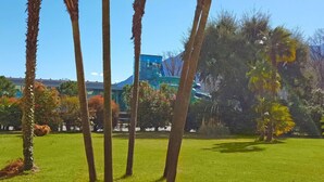 A well-maintained grassy area with palm trees and a modern building in the background. - Residenza Lido Appartment 009 by Interhome (Locarno)