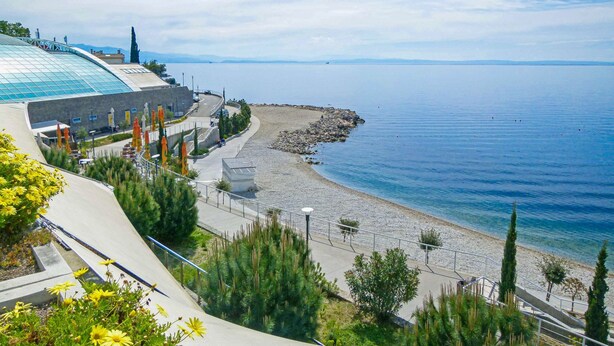 Ein Küstenhotel mit einer geschwungenen Glasfassade, einem Kiesstrand und freiem Blick auf das Meer.