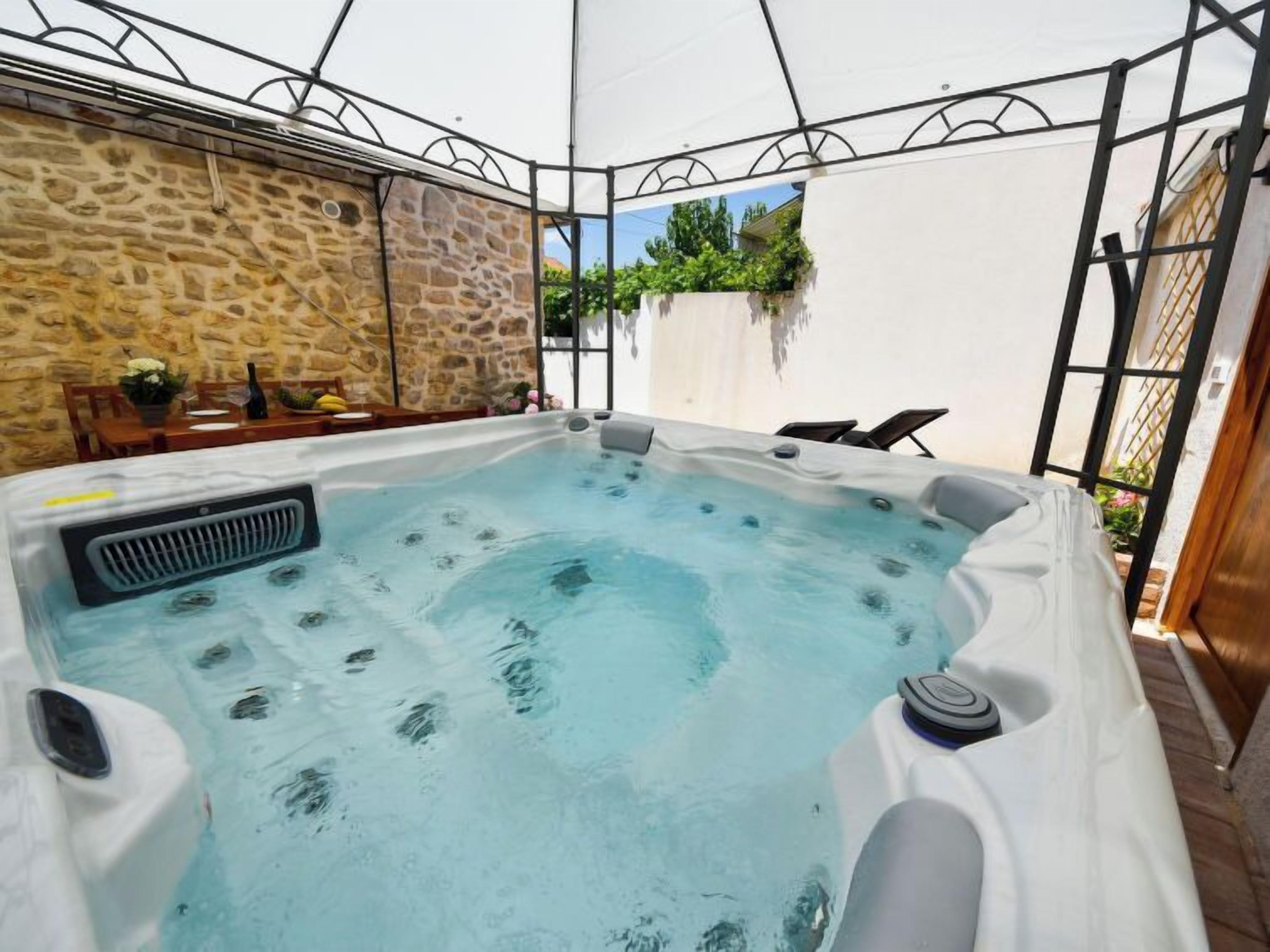 Ein Whirlpool in einer überdachten Außenbereich mit Steinwänden und einem Tisch mit Blumen.