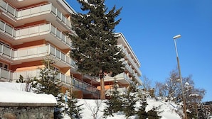 Monikerroksinen hotelli, jossa on parvekkeet, lumipeitteinen maisema ja kirkas, sininen taivas.