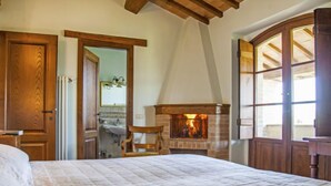 A bedroom with a large bed, a wooden ceiling, a fireplace, and a bathroom visible through an open door. - Allerona by Interhome (Orvieto)