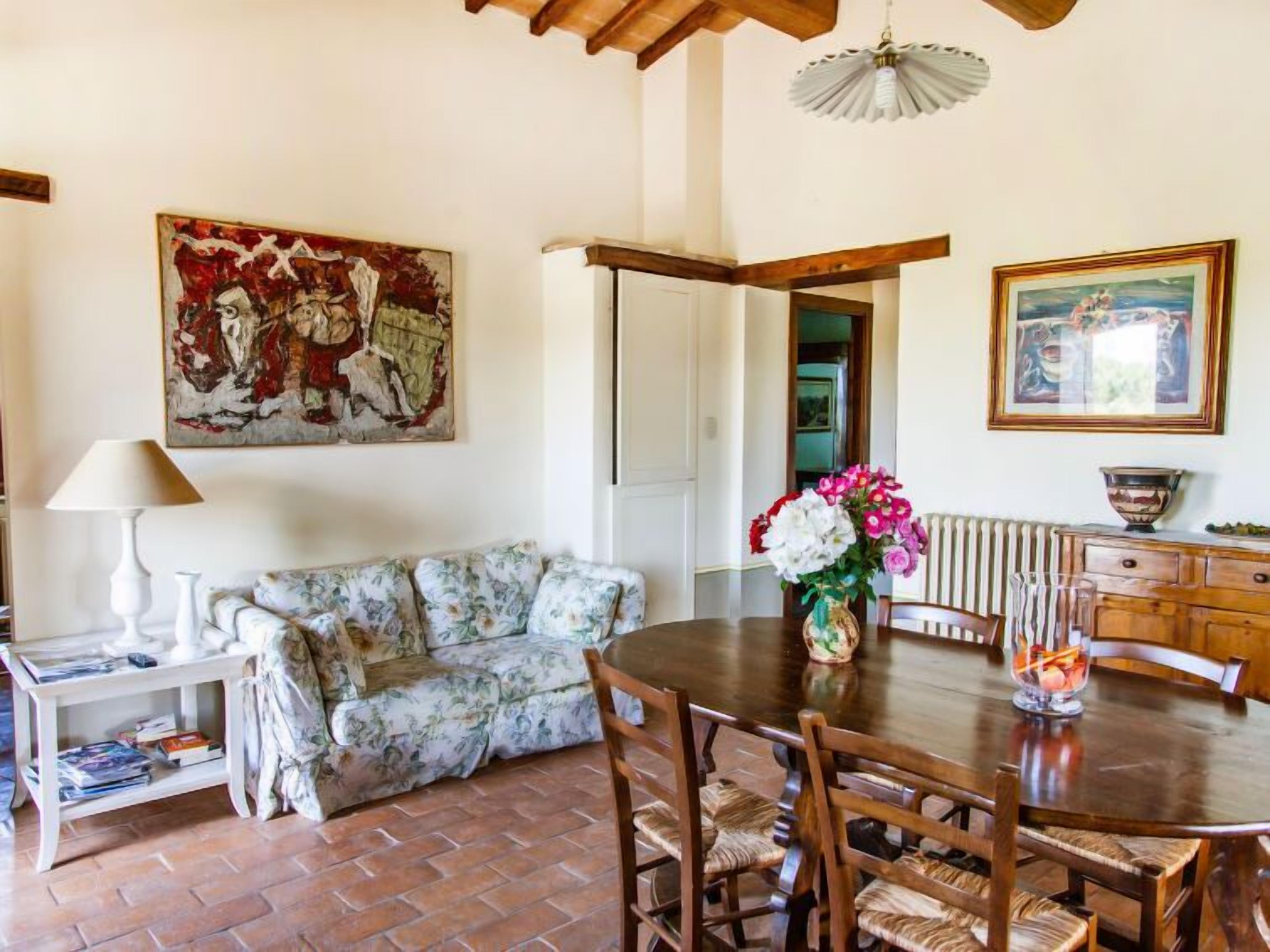 Un área de comedor con una mesa redonda de madera, un sofá floral y un cuadro en la pared.