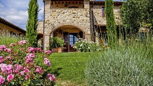 A stone building with a tiled roof, an arched entrance, and a well-maintained garden with pink roses. - Allerona by Interhome (Orvieto)