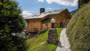 A wooden chalet with a stone pathway leading to the entrance, surrounded by greenery and a clear sky. - Pinot Gris combles by Interhome (Verbier)