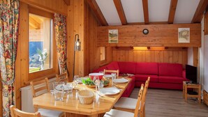 A wooden interior with a dining table set for four, a red sofa, and a television on a small table. - Pinot Gris combles by Interhome (Verbier)