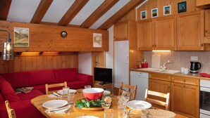 A cozy cabin-style room with a wooden dining table set for four, a red sofa, and a kitchen area with wooden cabinets and a coffee maker. - Pinot Gris combles by Interhome (Verbier)