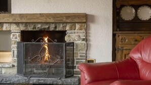 Une cheminée en pierre avec un foyer en métal, un fauteuil en cuir et un buffet en bois orné d’assiettes décoratives.