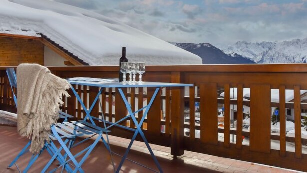 Un balcon avec une table et des chaises, donnant sur un paysage montagneux enneigé.
