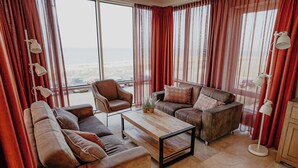 A spacious living room with a large window, leather sofas, a wooden coffee table, and red curtains. - De Zeeparel by Interhome (Egmond aan Zee)