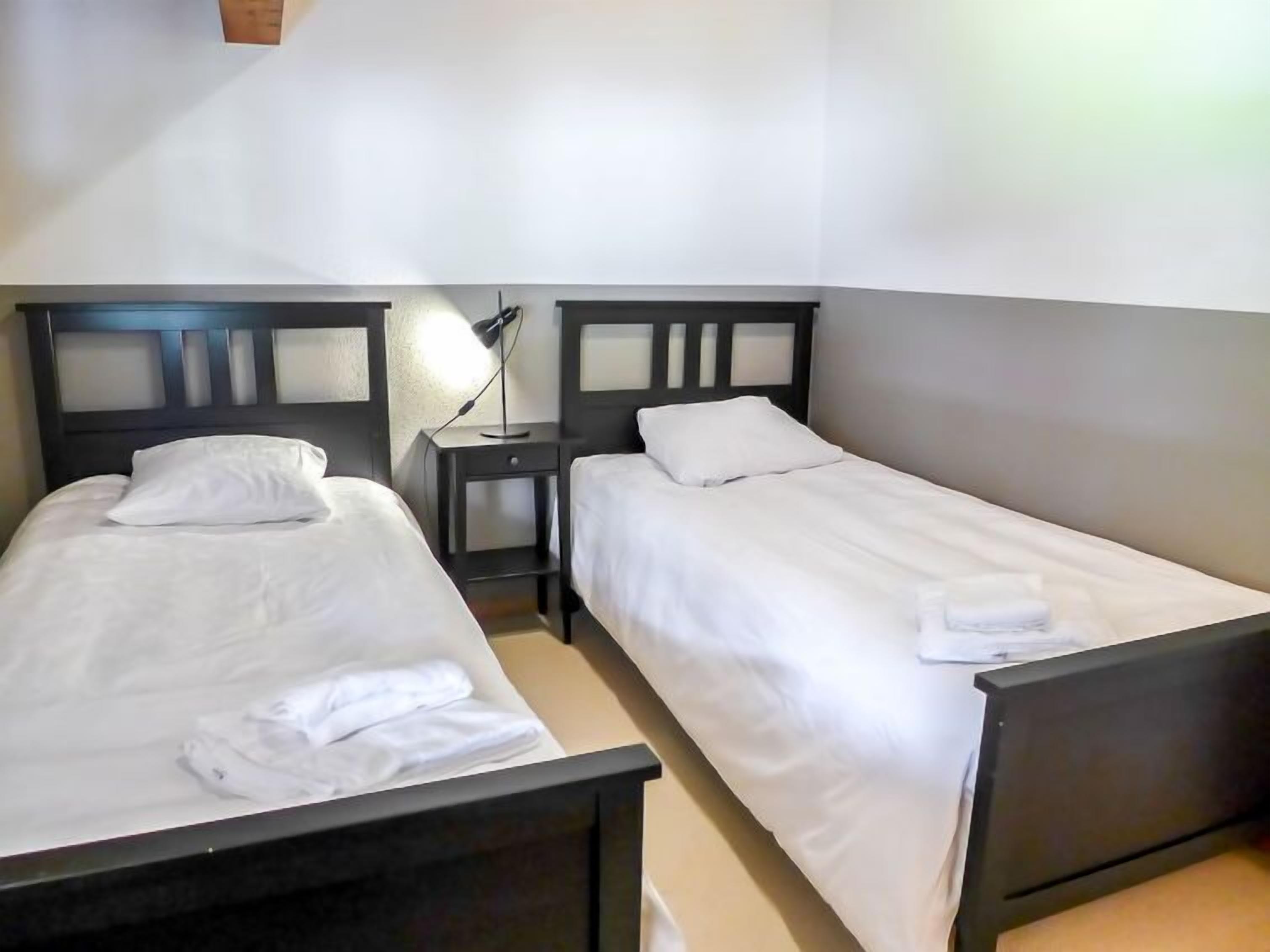 Une chambre double avec deux lits simples, une table de chevet avec une lampe et une petite table.