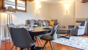 A modern dining area with a round table, chairs, and a sofa. There are two wall-mounted lamps, a radiator, and a window with blinds. - Villars Soleil B15 by Interhome (Villars)