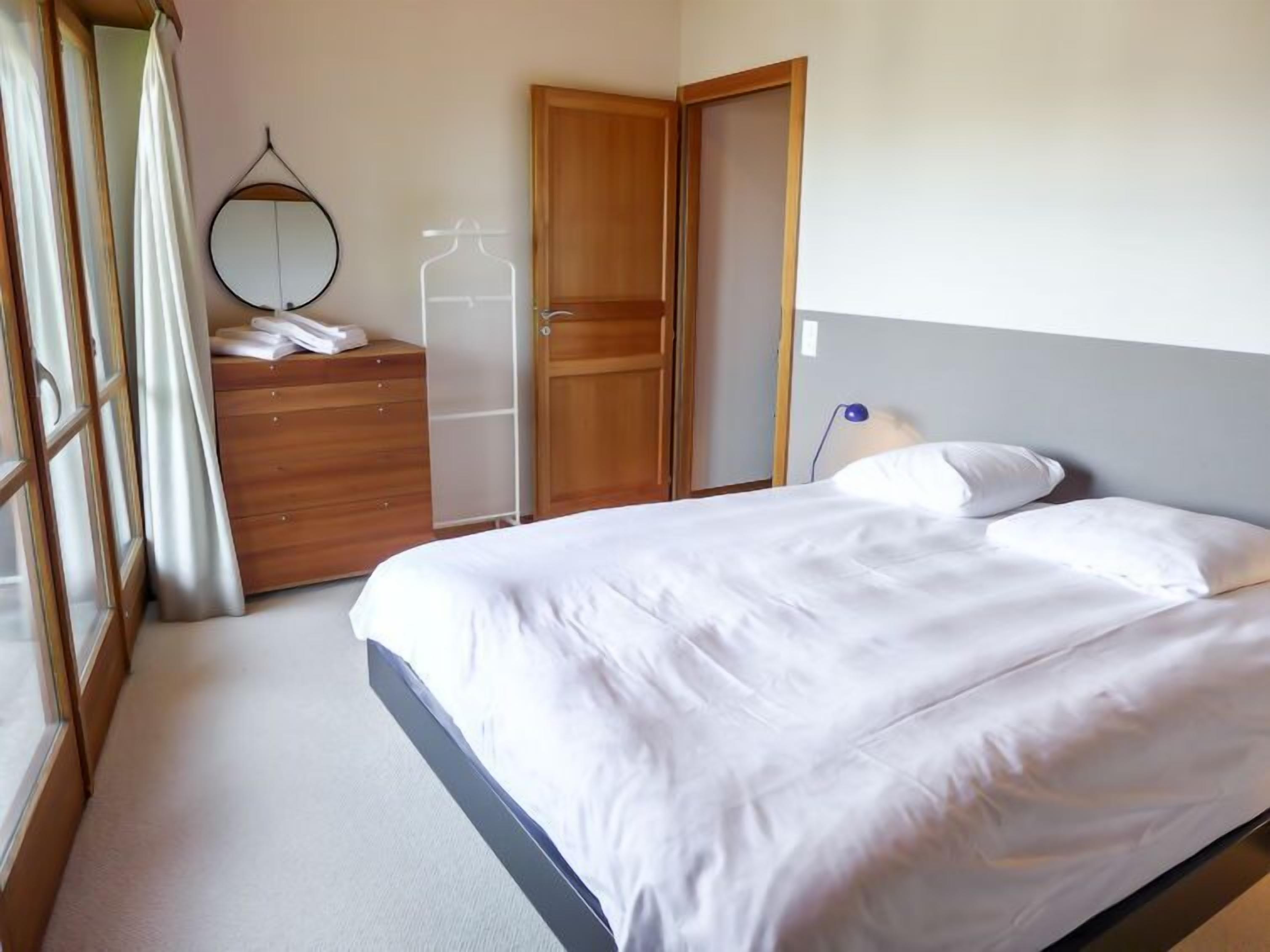 A bedroom with a bed, a wooden wardrobe, a mirror, and a door.