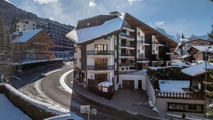 A multi-story building with balconies, a snow-covered street, and mountainous background. - Villars Soleil B15 by Interhome (Villars)