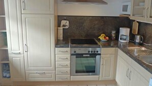 Una cocina compacta con armarios blancos, una campana de acero inoxidable, un horno integrado y un microondas.