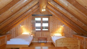 Una cabaña de madera acogedora con dos camas individuales, una mesita y una ventana con cortinas.