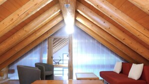 Una habitación en el ático con vigas de madera, un sofá rojo, una mesa de madera y una silla.