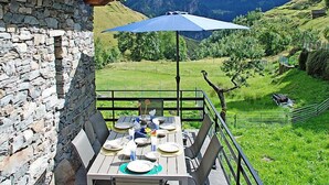 Una mesa al aire libre con vista a las montañas, un muro de piedra y una barandilla de metal.