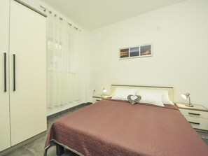 A bedroom with a bed, a nightstand, a bedside table, a wardrobe, and a window with curtains. - Snježana by Interhome (Karlobag)
