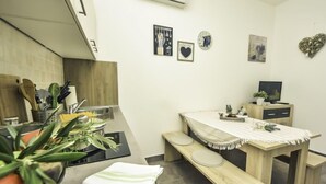 A compact kitchen with modern appliances, a dining area with a bench, and a small TV on a wooden cabinet. - Snježana by Interhome (Karlobag)