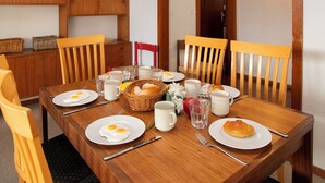 A dining table set with breakfast items including eggs, bread, and beverages, surrounded by wooden chairs and a wooden cabinet with baskets.